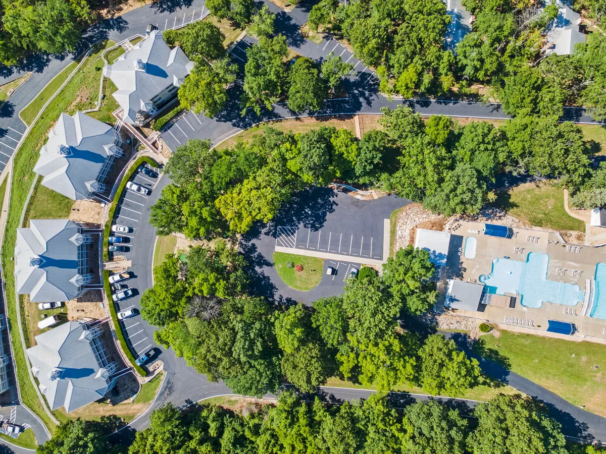 This exterior image captures the resort’s swimming pool surrounded by lush trees, nearby buildings, and open walkways. The visible pathways and green spaces create a sense of accessibility for walks and outdoor exploration, making this an ideal setting for guests traveling with dogs.