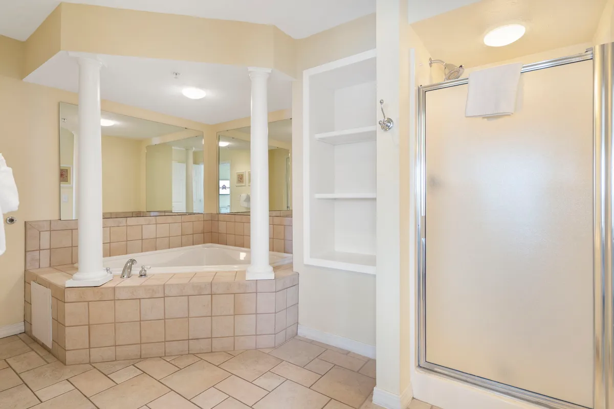 A luxurious ensuite bathroom with a large jetted jacuzzi tub, separate shower stall, elegant pillars, and a mirrored wall. The space feels inviting for relaxation and self-care.