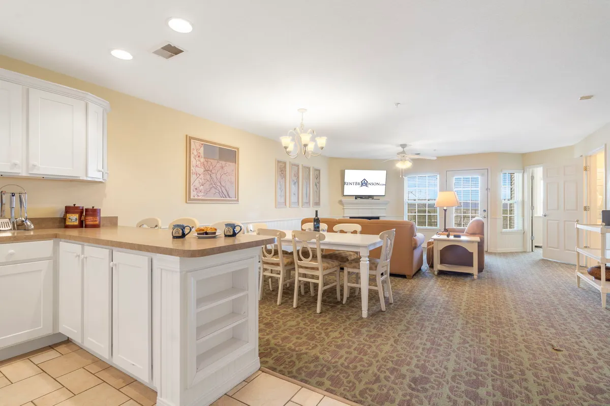 This interior image features a well-lit, open-concept space that seamlessly combines a kitchen with an island, a dining table, and a spacious living area with comfortable seating and a television. The kitchen and dining spaces are connected visually and physically, inviting family and guests to gather, cook, and relax together.