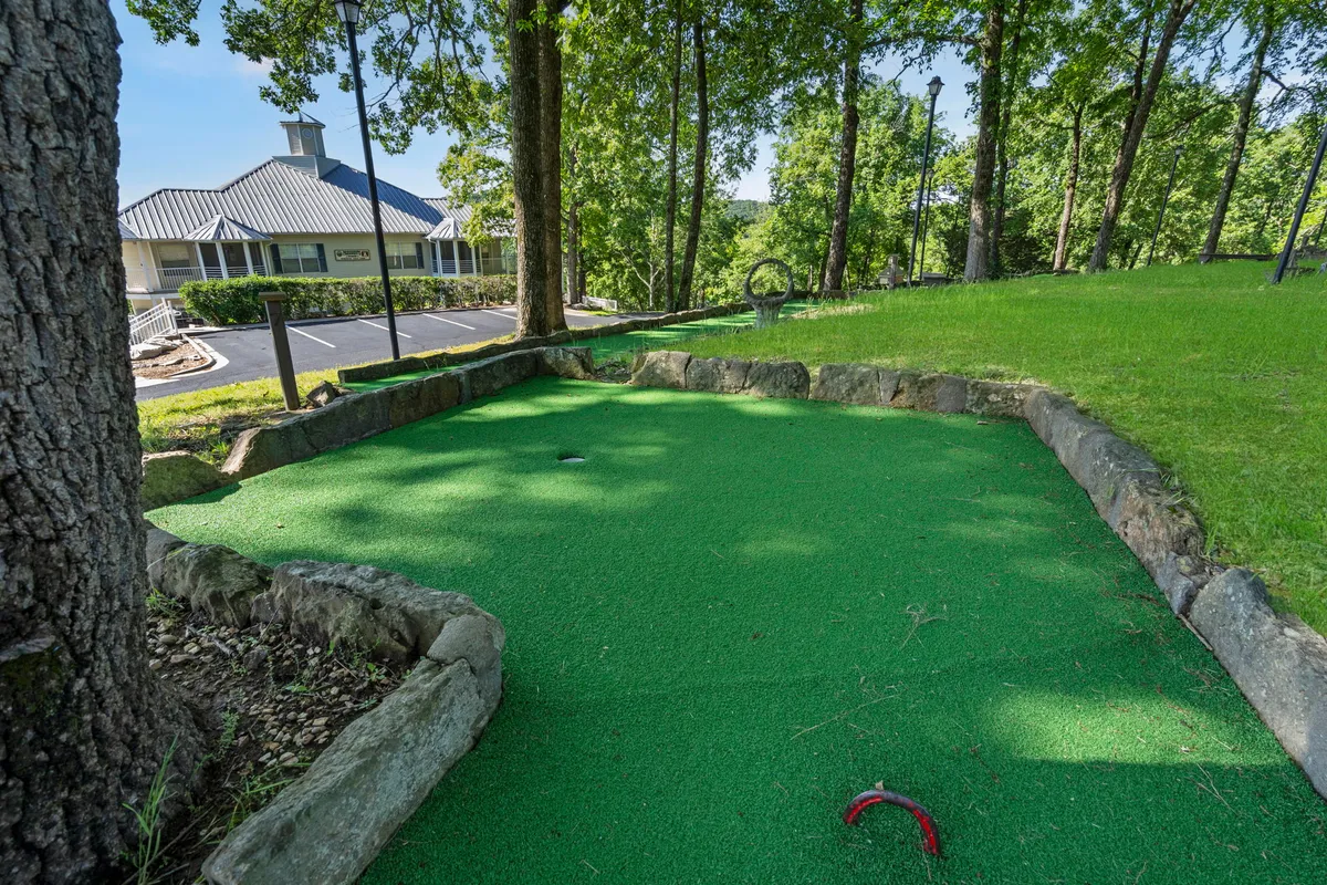 A playful exterior shot of the resort's mini-golf area, showcasing lush green grass, natural stone edging, and tall surrounding trees. Families are gathered around, enjoying a round of mini-golf in the fresh air.