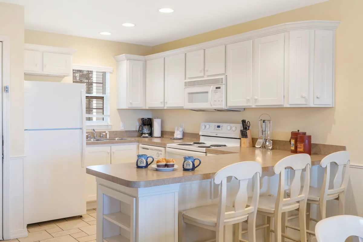 A bright, modern kitchen with white cabinetry, a functional island with seating, and up-to-date appliances. The space is designed for cooking, casual dining, and socializing, all while remaining part of the main living area.