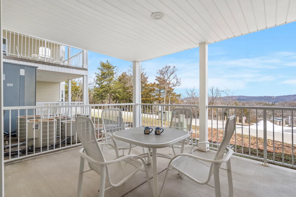 A cozy exterior patio scene with a table set for two, coffee mugs in place, surrounded by trees and offering a mountain view in the distance. The intimate setting suggests a peaceful spot to relax after a day outdoors.