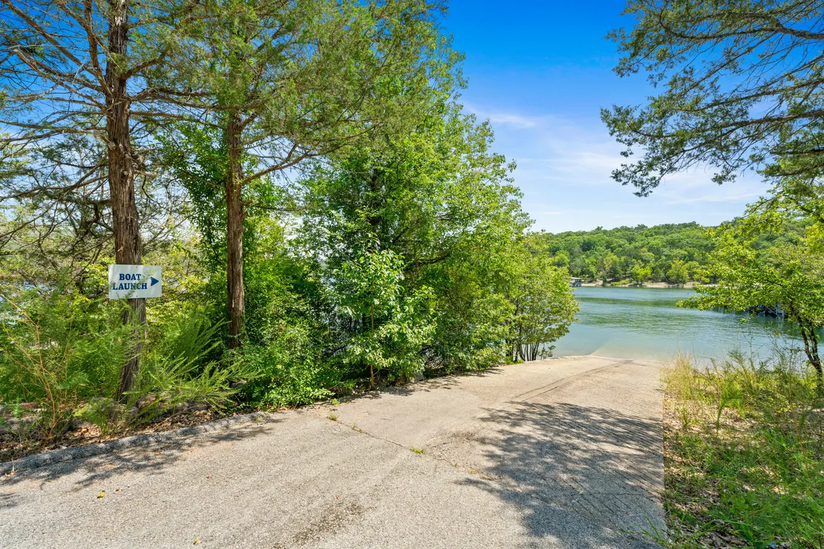 A waterfront scene with a clearly marked boat launch sign, calm lake waters, and trees lining the shore. The atmosphere is relaxed, hinting at both the beginning of a boating adventure and a spot for lakeside relaxation with pets or loved ones.