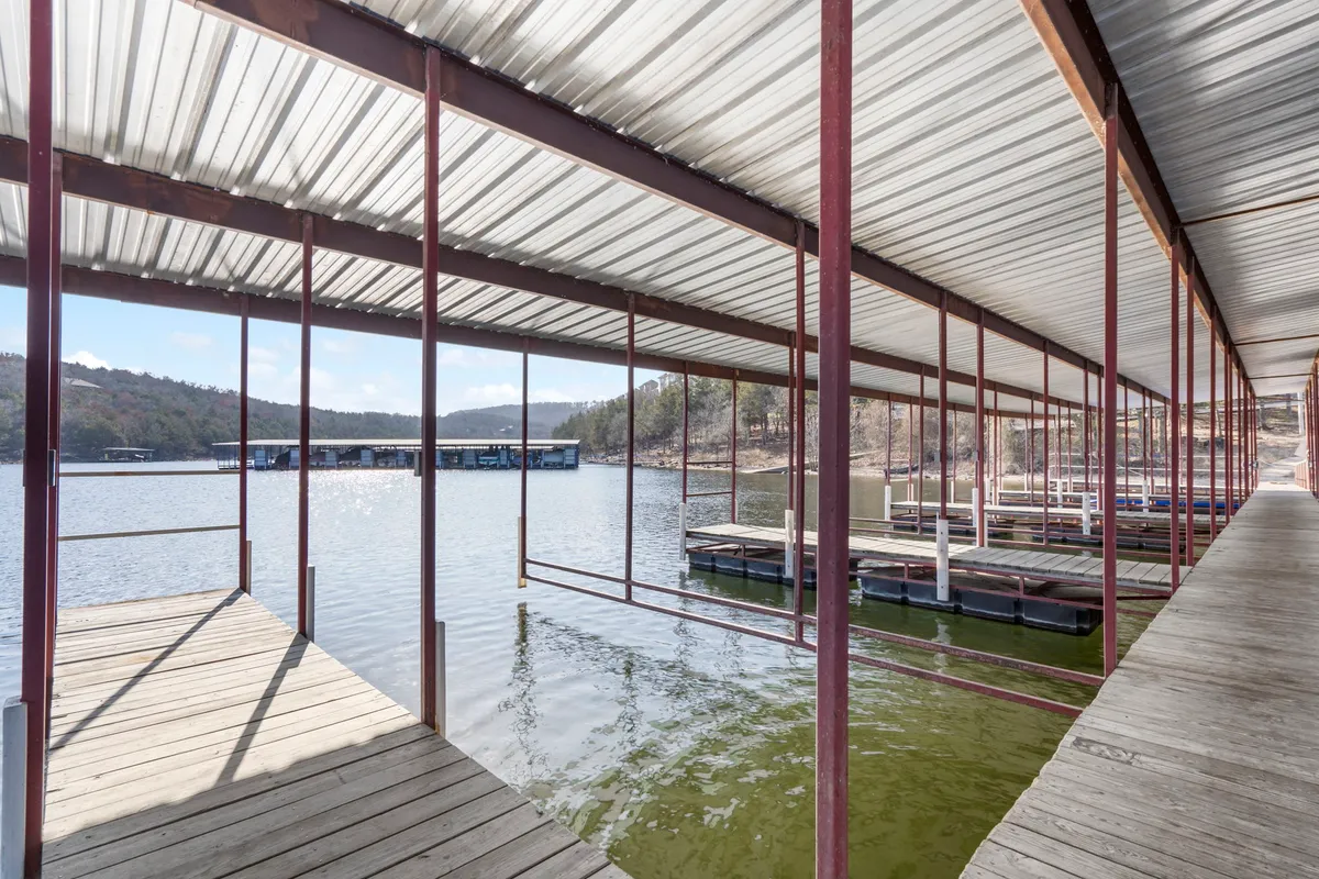 A serene view of Table Rock Lake with several boathouses and docks extending into tranquil water, set against a backdrop of gentle mountains. The scene captures the essence of lakeside living with facilities for boating and fishing, and the soft light hints at either early morning or dusk.