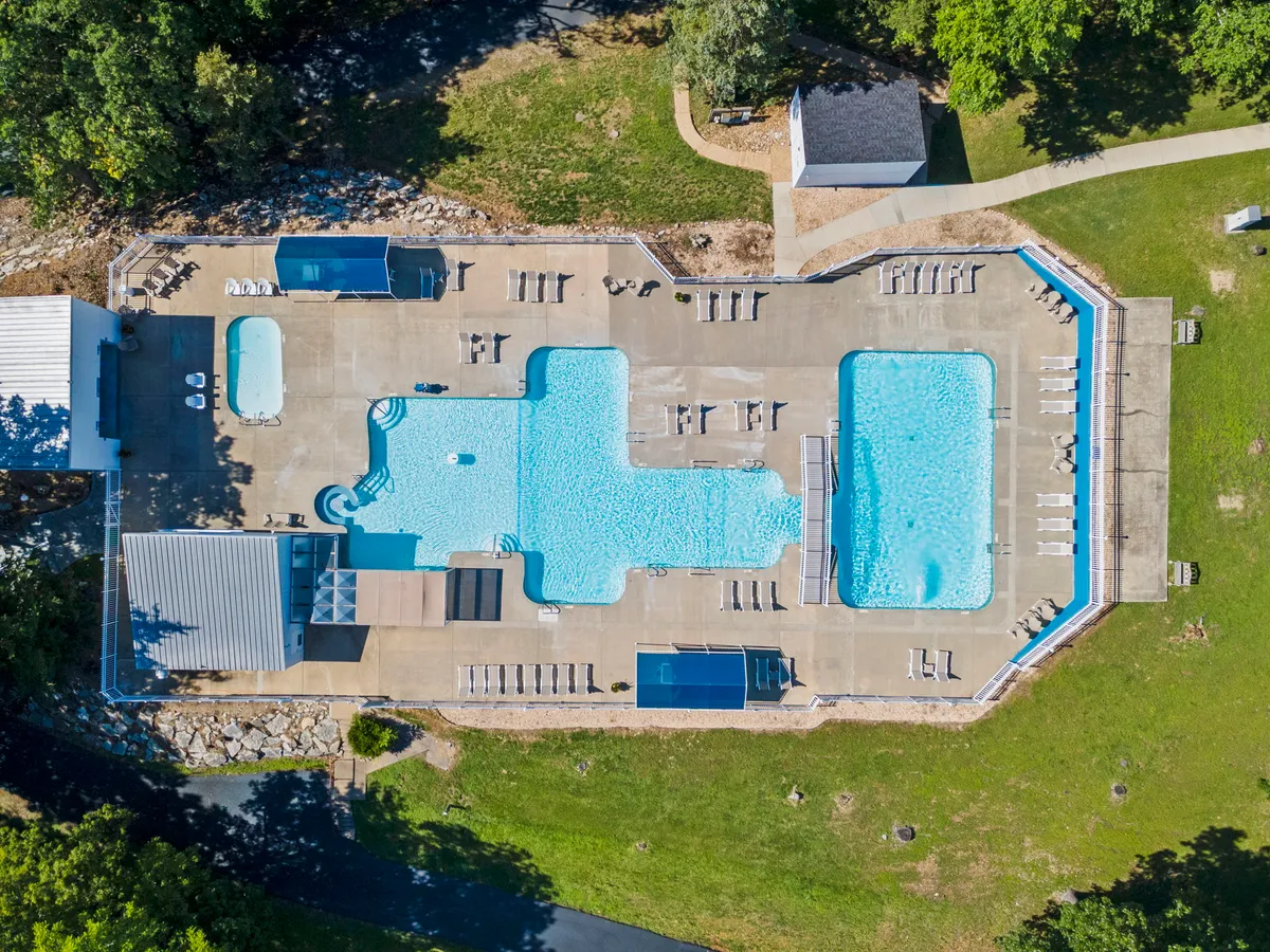 A bright, inviting outdoor swimming pool surrounded by lounge chairs and lush greenery, with guests swimming and relaxing. The lively atmosphere is perfect for summer days spent poolside.