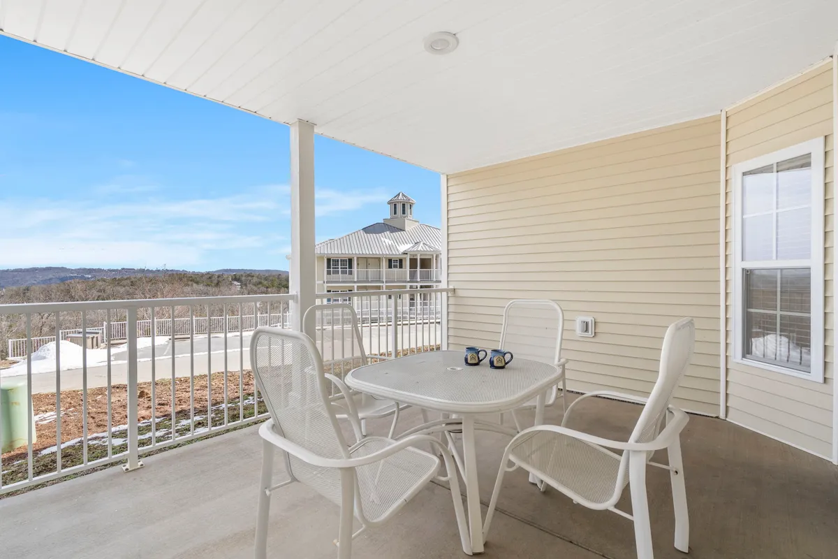 An inviting outdoor patio space with a table set for two, each with a coffee mug, overlooking a peaceful landscape framed by a railing. The tranquil scene suggests a perfect spot for couples or friends to unwind, take in morning views, or enjoy a quiet evening drink together.